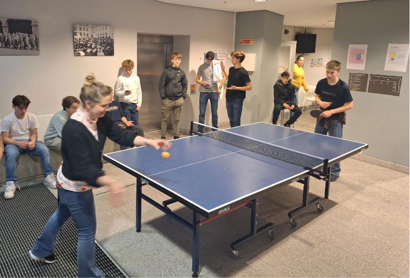 en person som spiller bordtennis i et rom med andre mennesker