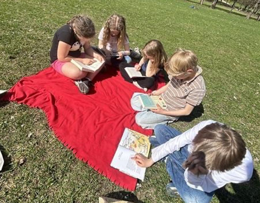 en gruppe mennesker som sitter på et teppe på en gresskledd ås